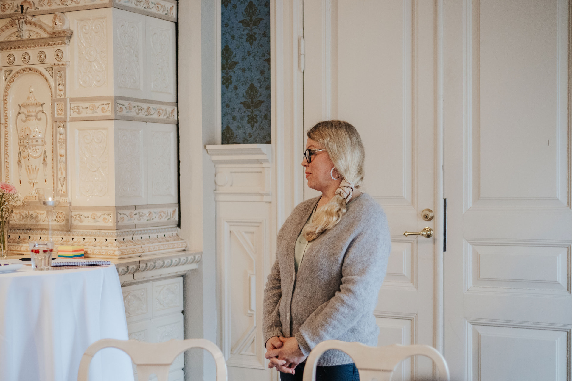 Saija Salo valoisaan huoneeseen, valkoisen kaakeliuunun ja peilioven vieressä